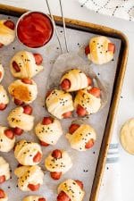 Baking sheet filled with baked mini pigs in a blanket served with ketchup and dijon mustard.