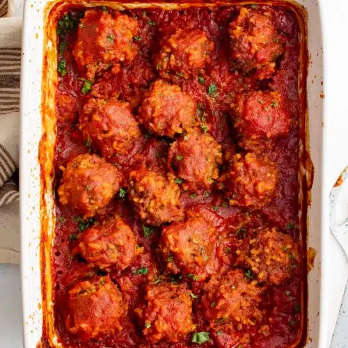Large white baking pan filled with cooked porcupine meatballs in a hearty tomato sauce.