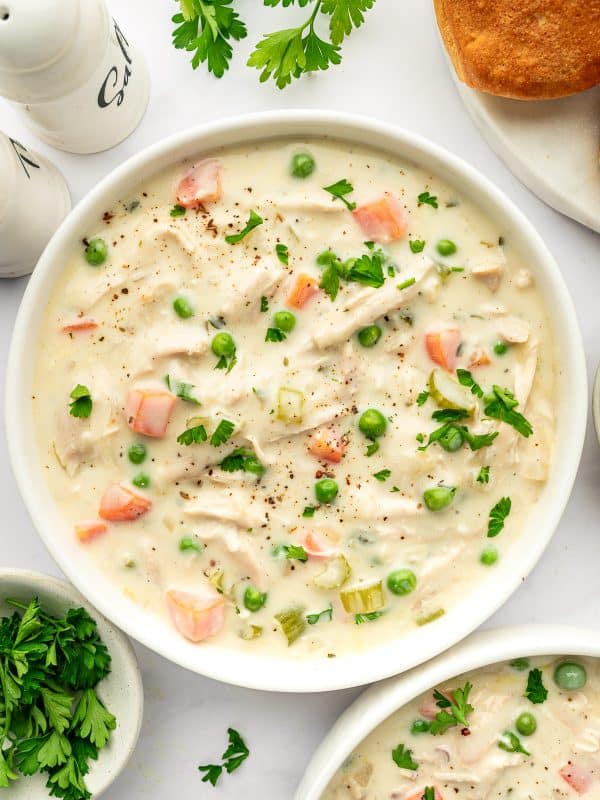 Bowl of Chicken Pot Pie Soup garnished with parsley and cracked pepper, served with biscuits on the side.