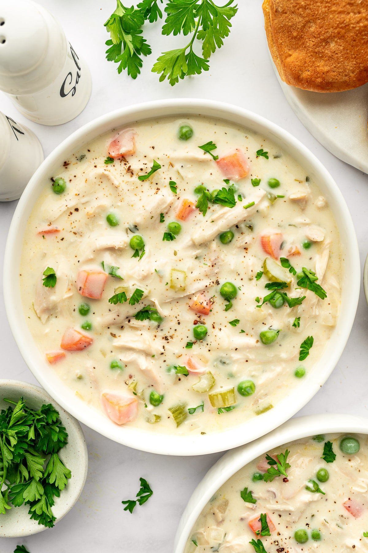 Bowl of Chicken Pot Pie Soup garnished with parsley and cracked pepper, served with biscuits on the side.