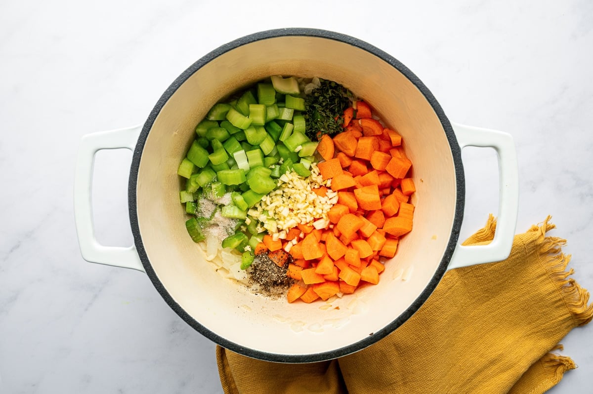 Chopped carrots, celery, garlic, and seasonings in a Dutch oven before cooking.