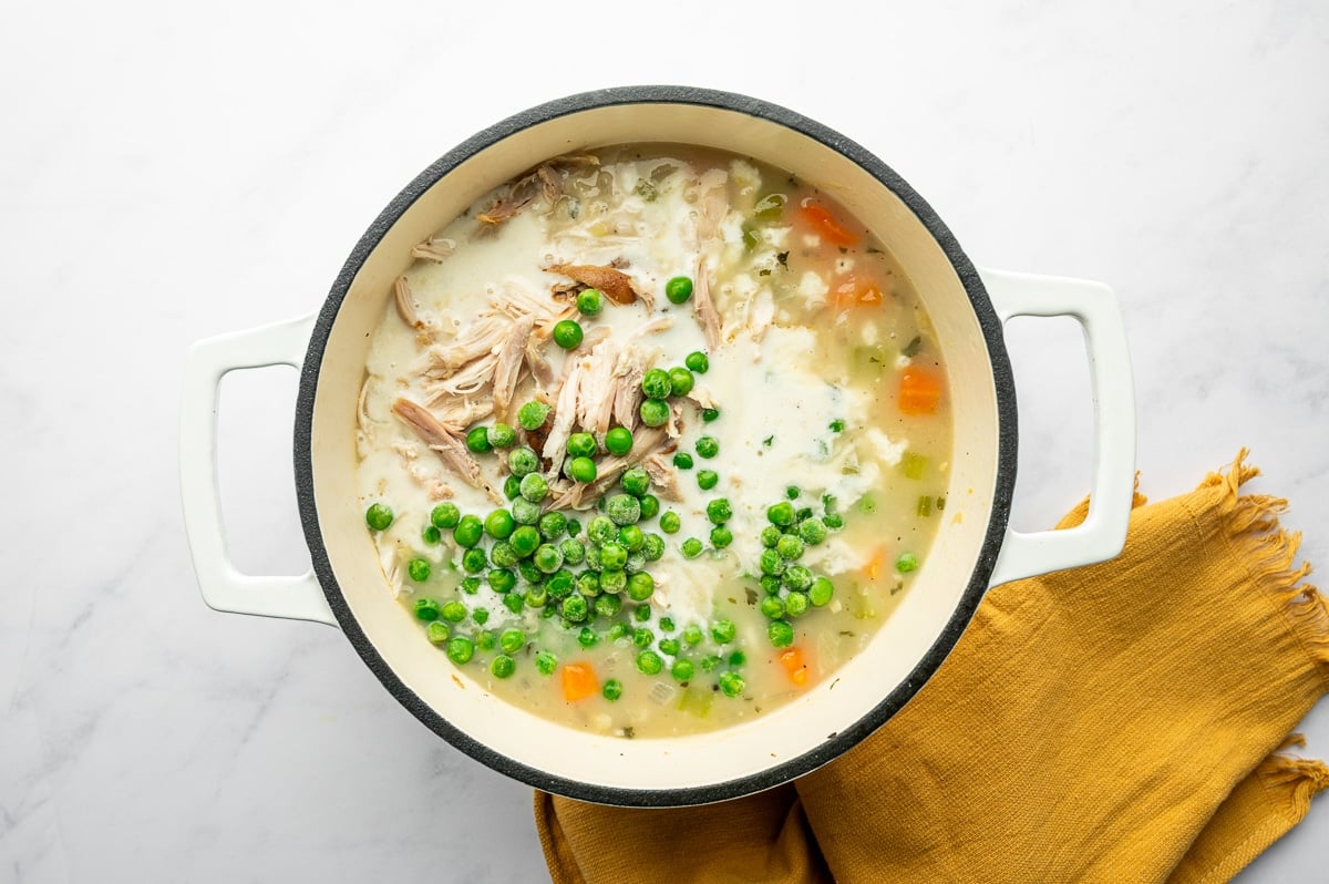 Shredded chicken and green peas added to a creamy soup base in a Dutch oven.