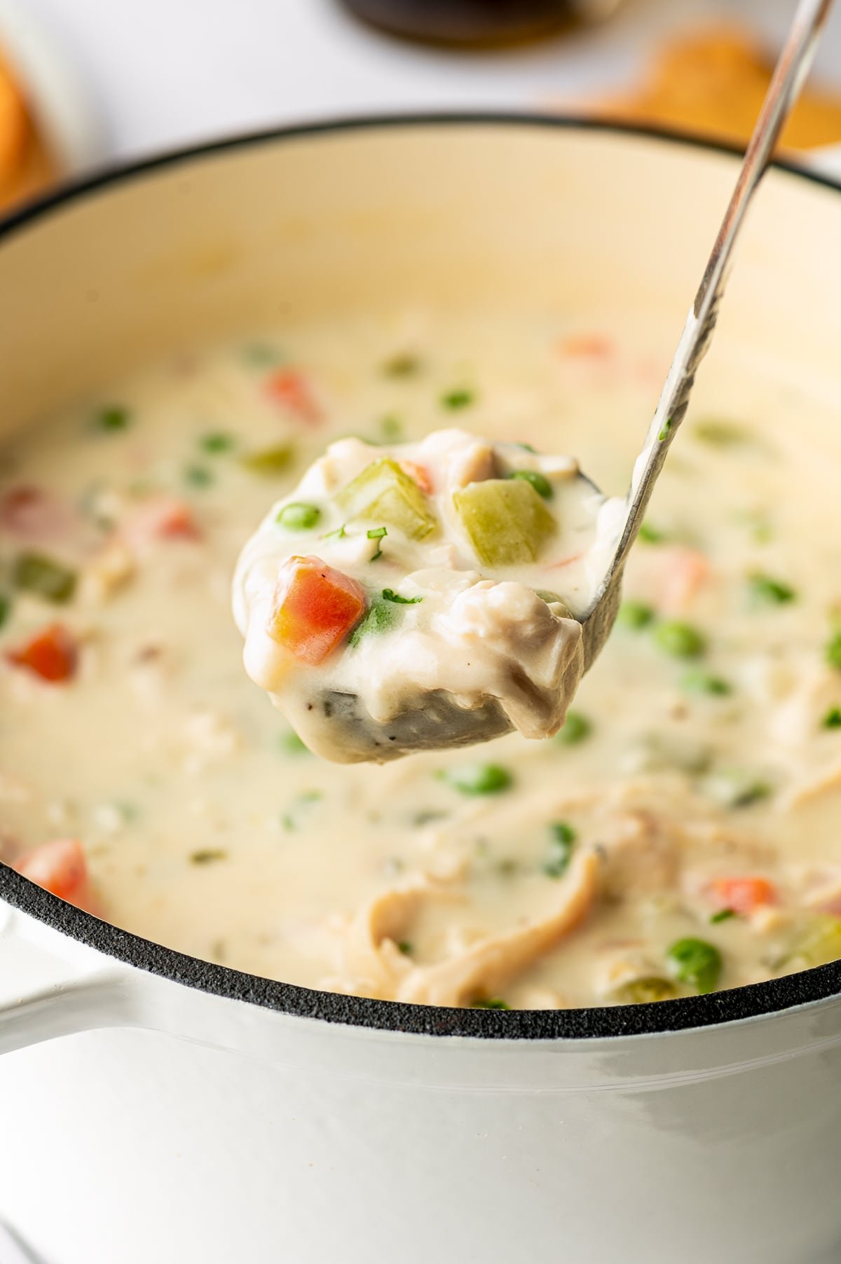 A ladle lifting a scoop of creamy Chicken Pot Pie Soup filled with chicken, carrots, celery, and peas.