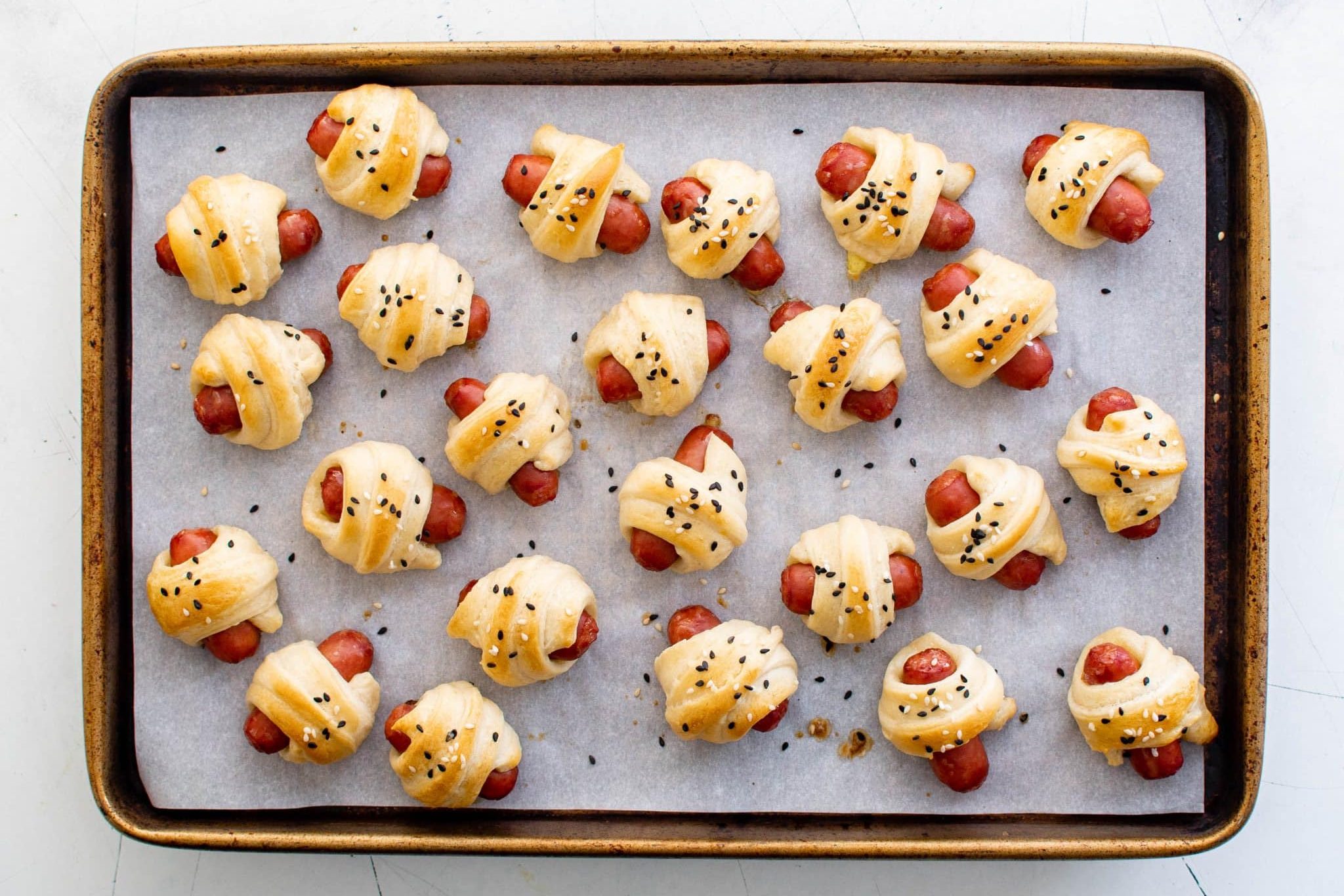 Golden brown pigs in a blanket baked with sesame seeds on a sheet pan
