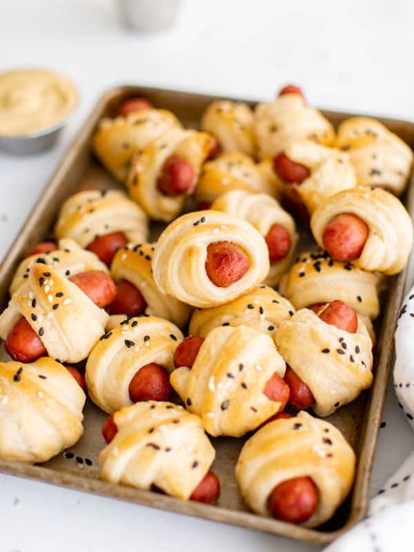 Tray of freshly baked pigs in a blanket with flaky crescent dough and sesame seeds