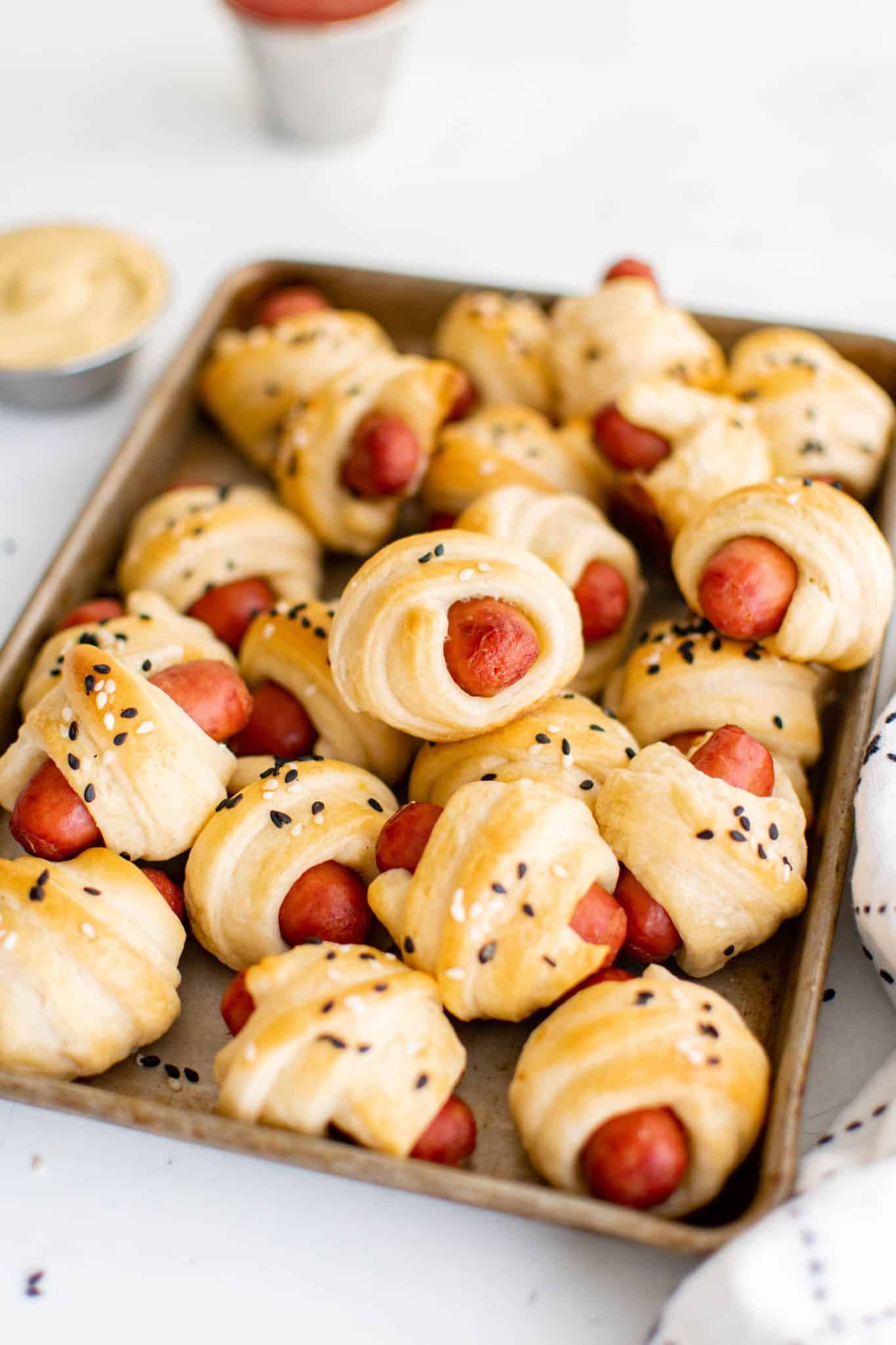 Tray of freshly baked pigs in a blanket with flaky crescent dough and sesame seeds