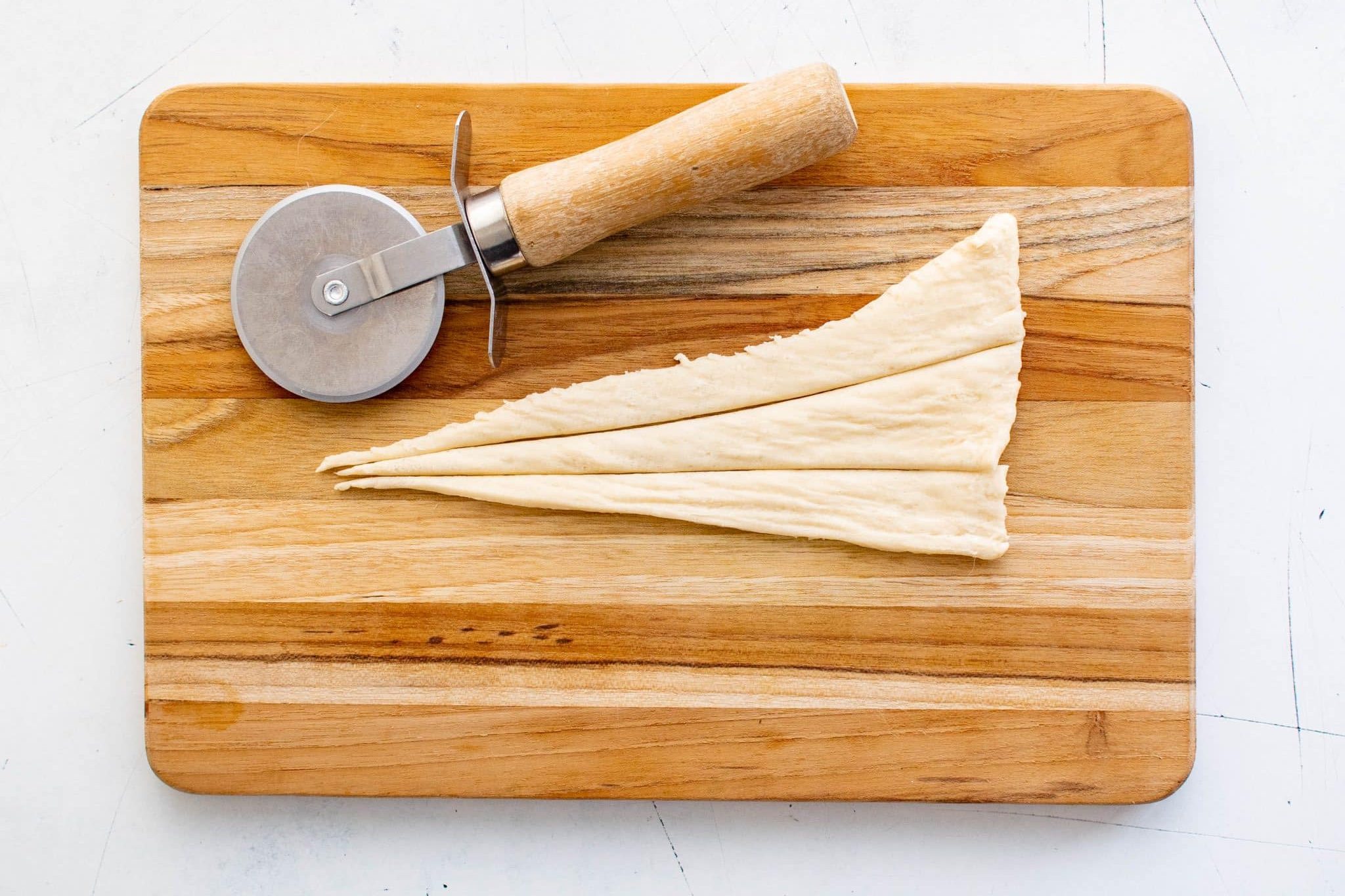 Crescent roll dough cut into long triangles on a wooden cutting board with a pizza cutter