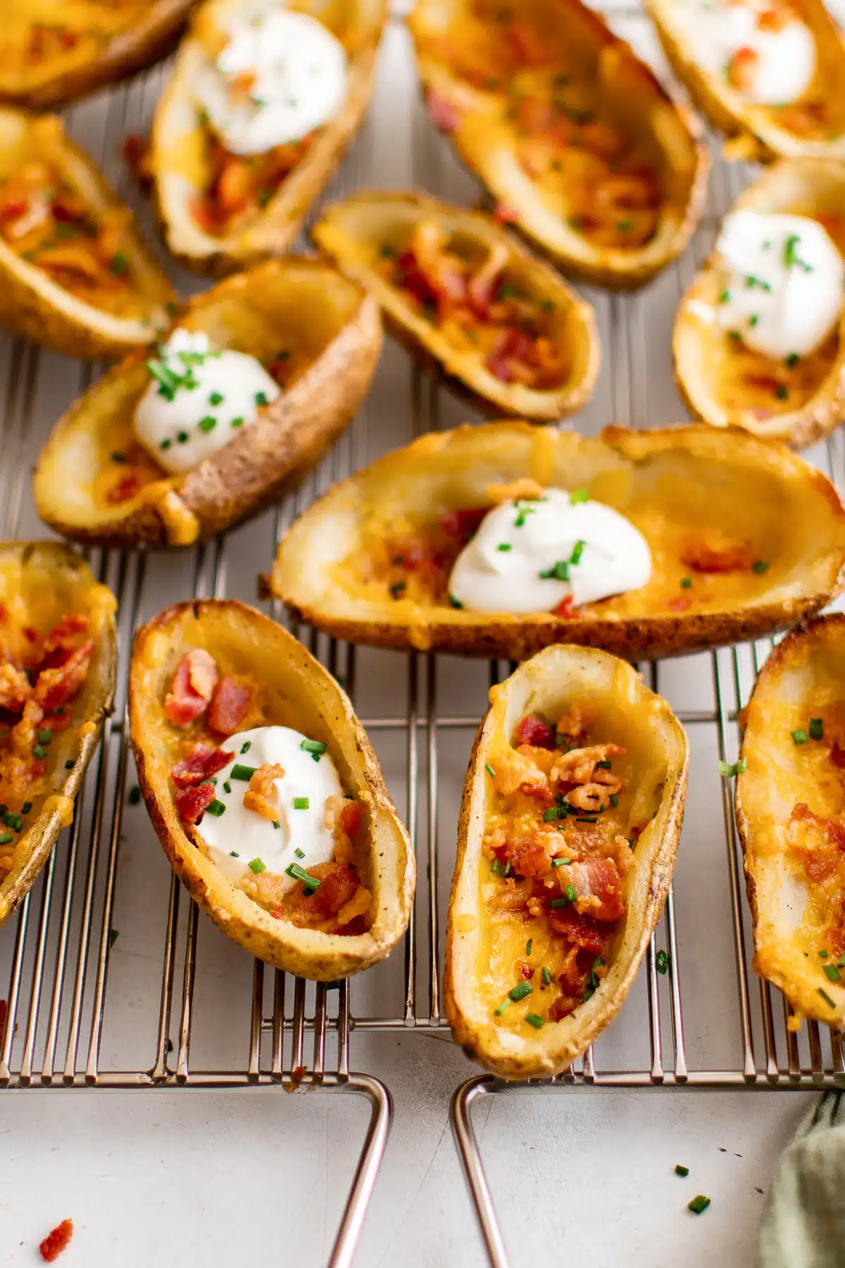 Potato skins filled with cheese, bacon, chives, and some with sour cream on a wire cooking rack.