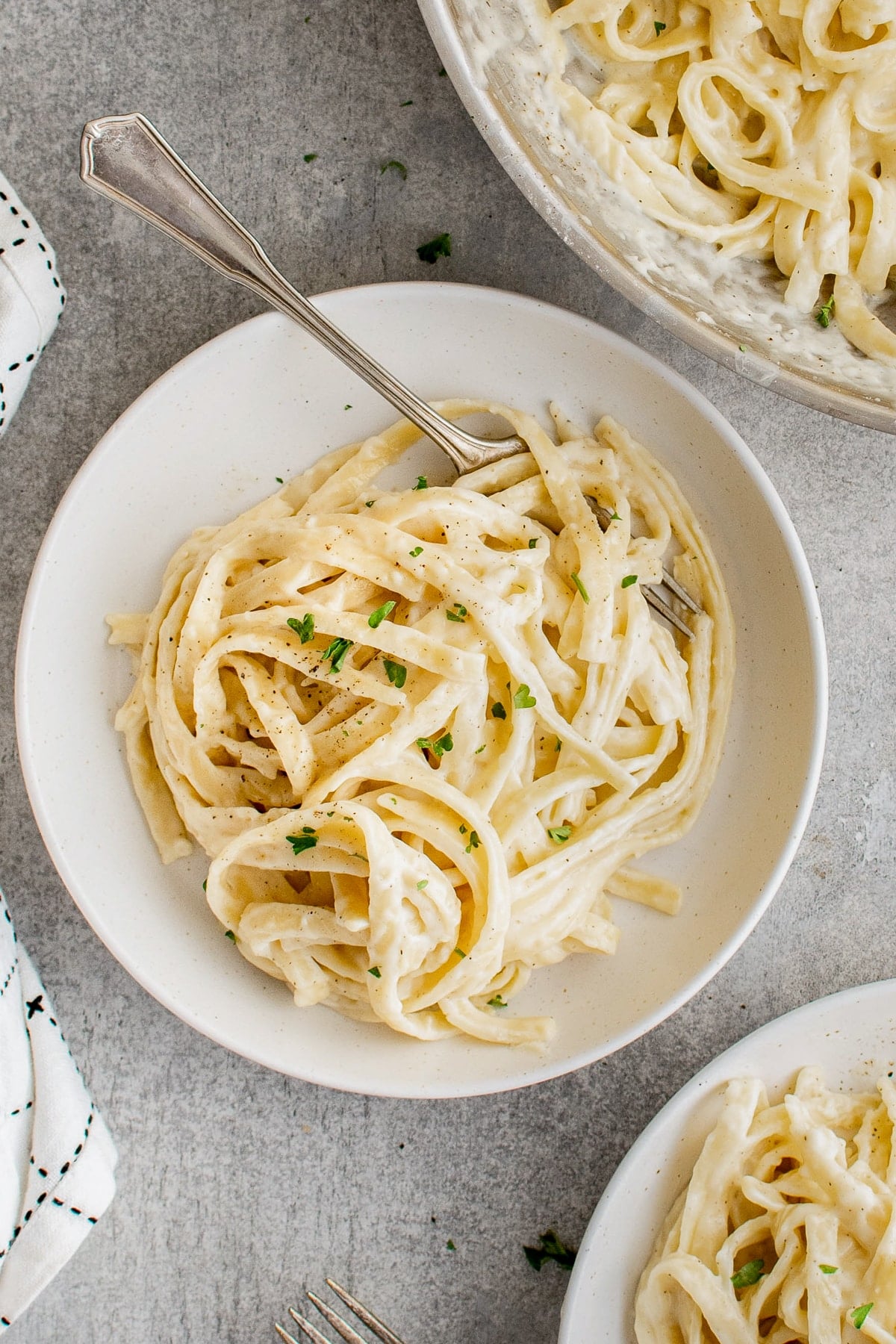 White plate with fettuccini noodles tossed in creamy Alfredo sauce and garnished with fresh parsley.