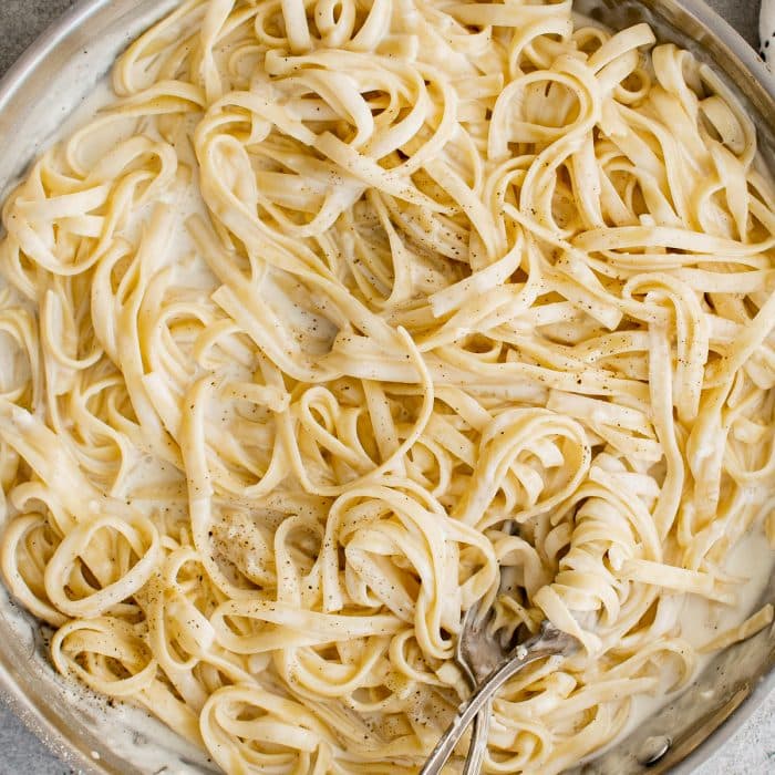 Large stainless steel skillet filled with cooked fettuccine noodles tossed in alfredo sauce.
