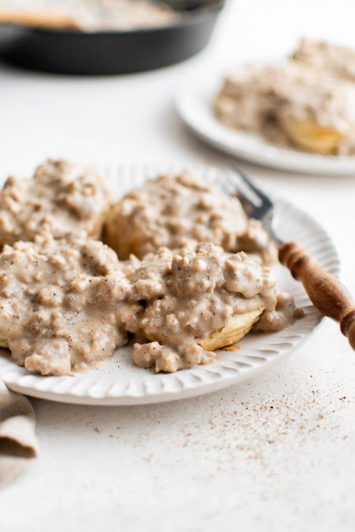 Plate of freshly baked biscuits smothered in creamy sausage gravy with a wooden-handled fork resting on the side.