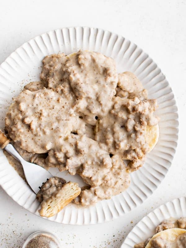 Overhead shot of biscuits covered in sausage gravy with a fork resting on the plate.
