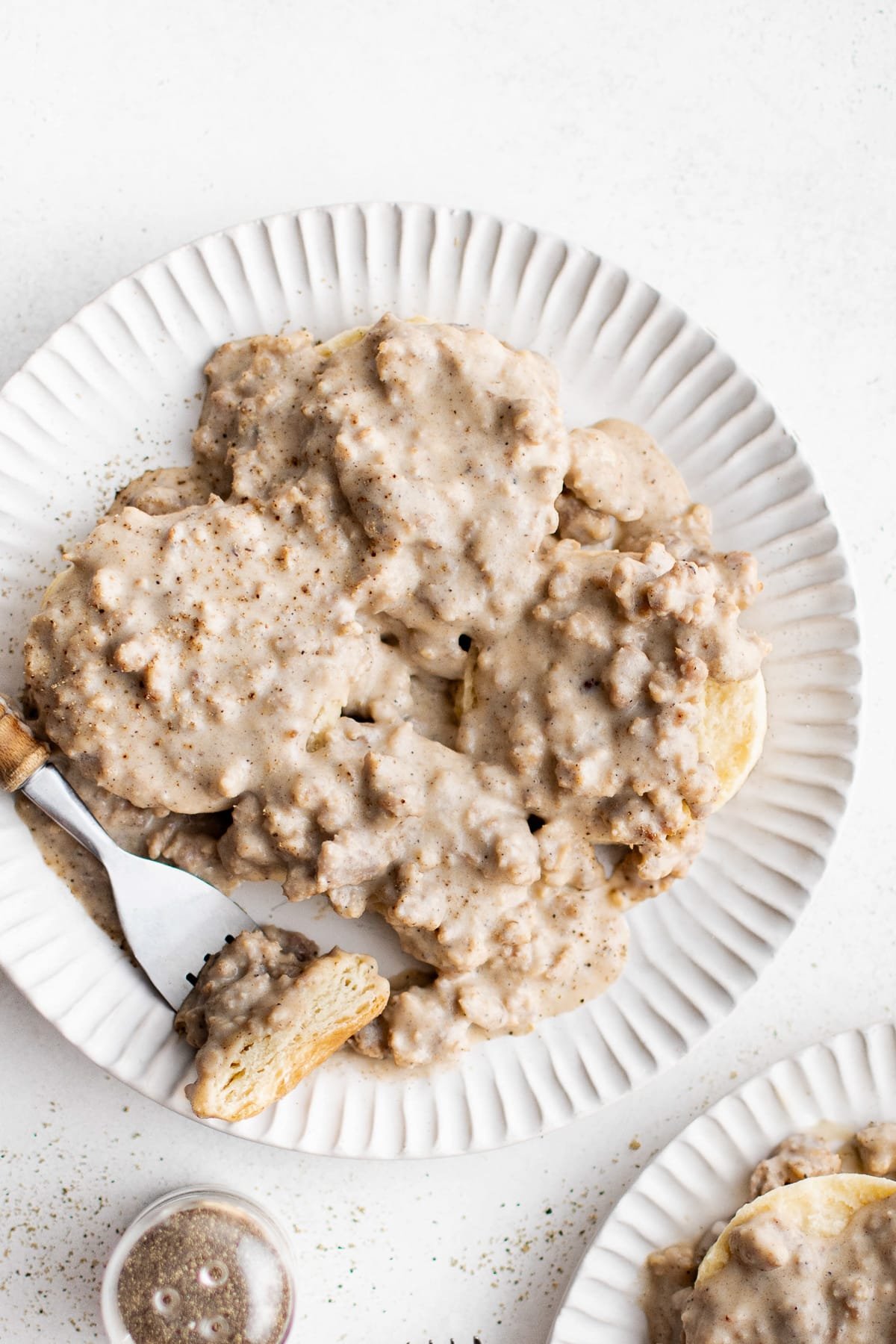 Overhead shot of biscuits covered in sausage gravy with a fork resting on the plate.
