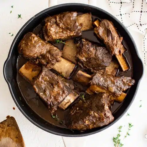 Large white dutch oven filled with tender cooked braised beef short ribs with a red wine beef gravy.