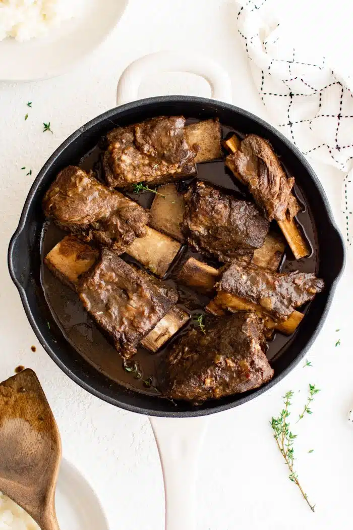 Large white Dutch oven filled with tender cooked braised beef short ribs with red wine beef gravy.