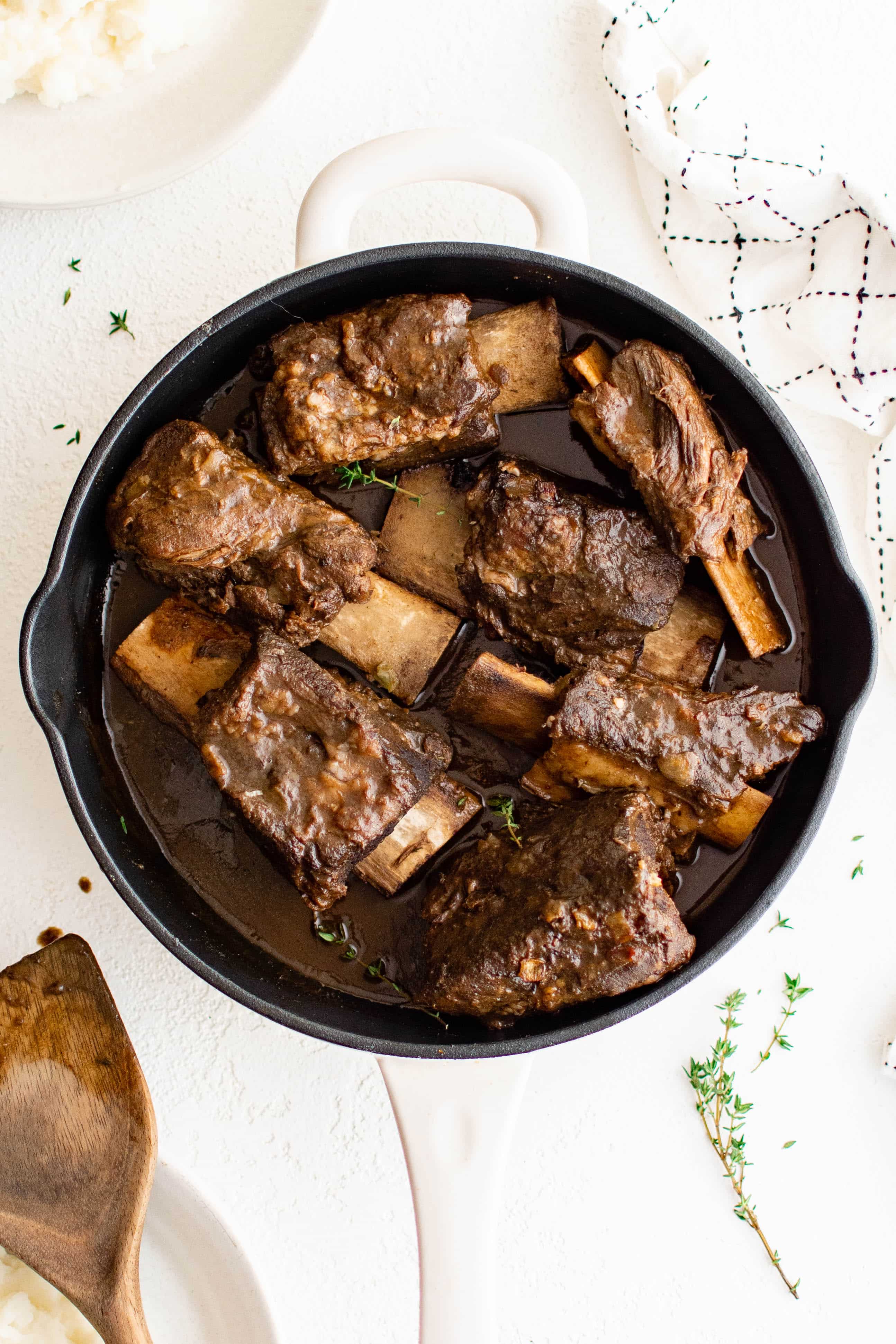 Large white dutch oven filled with tender cooked braised beef short ribs with a red wine beef gravy.