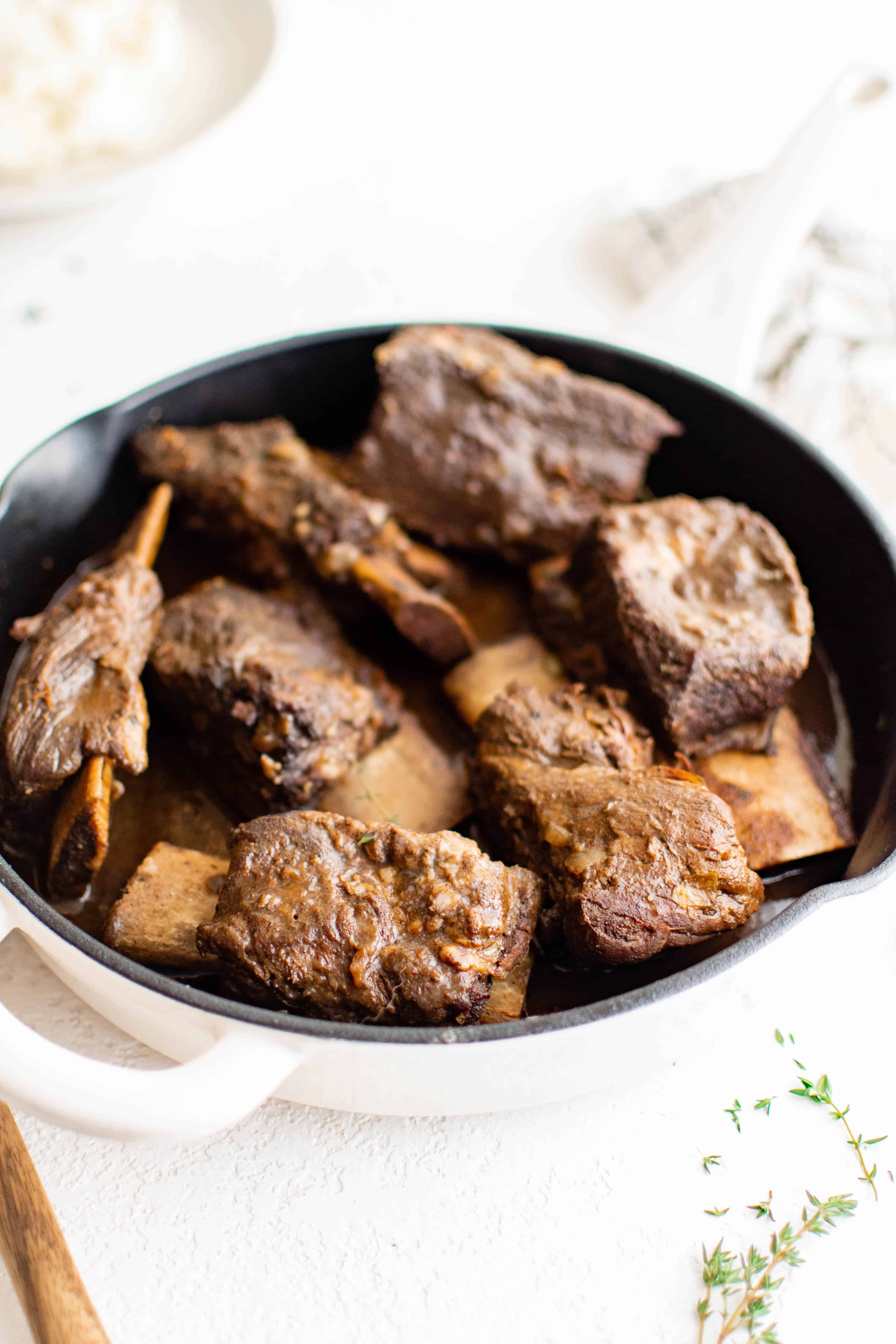 Large white dutch oven filled with tender cooked braised beef short ribs with a red wine beef gravy.