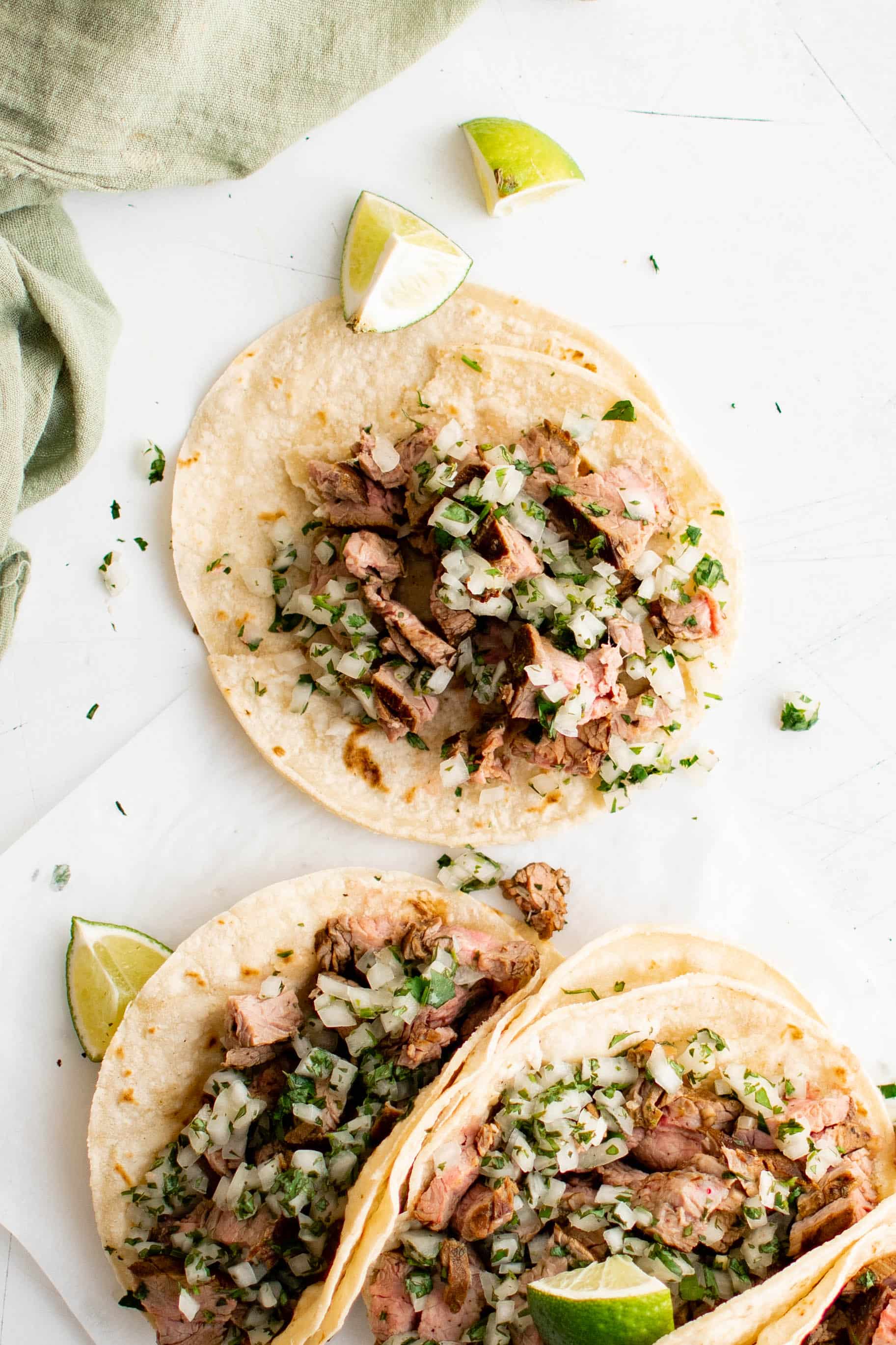 Several carne asada tacos made with corn tortillas and topped with a fresh onion, cilantro, and lime juice salsa.
