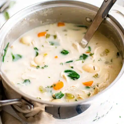 Stainless steel soup pot filled with creamy chicken and gnocchi soup filled with carrots, celery, and fresh spinach.