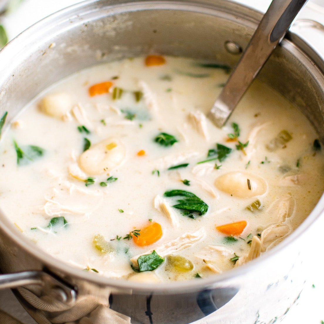 Stainless steel soup pot filled with creamy chicken and gnocchi soup filled with carrots, celery, and fresh spinach.