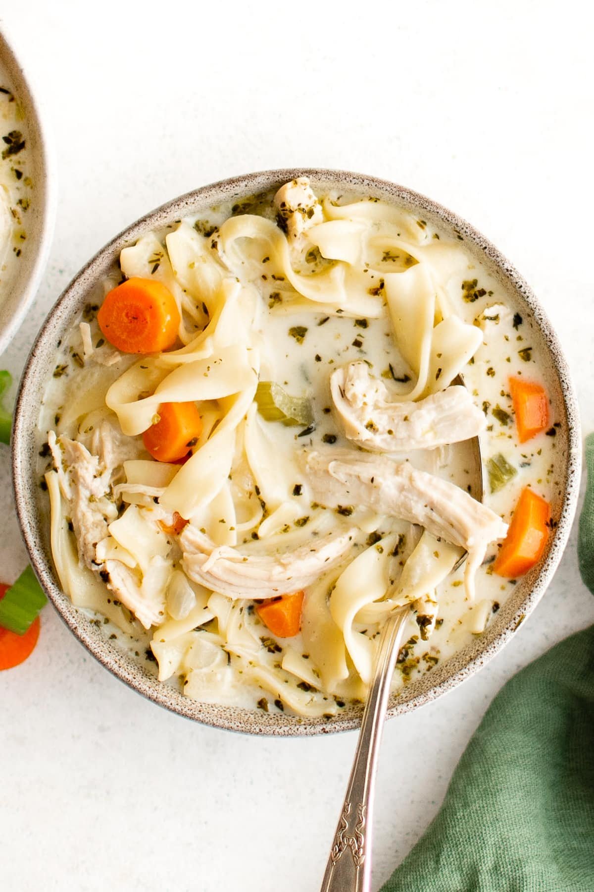 White soup bowl filled with carrots, shredded chicken, celery, and noodles, in a creamy chicken broth.