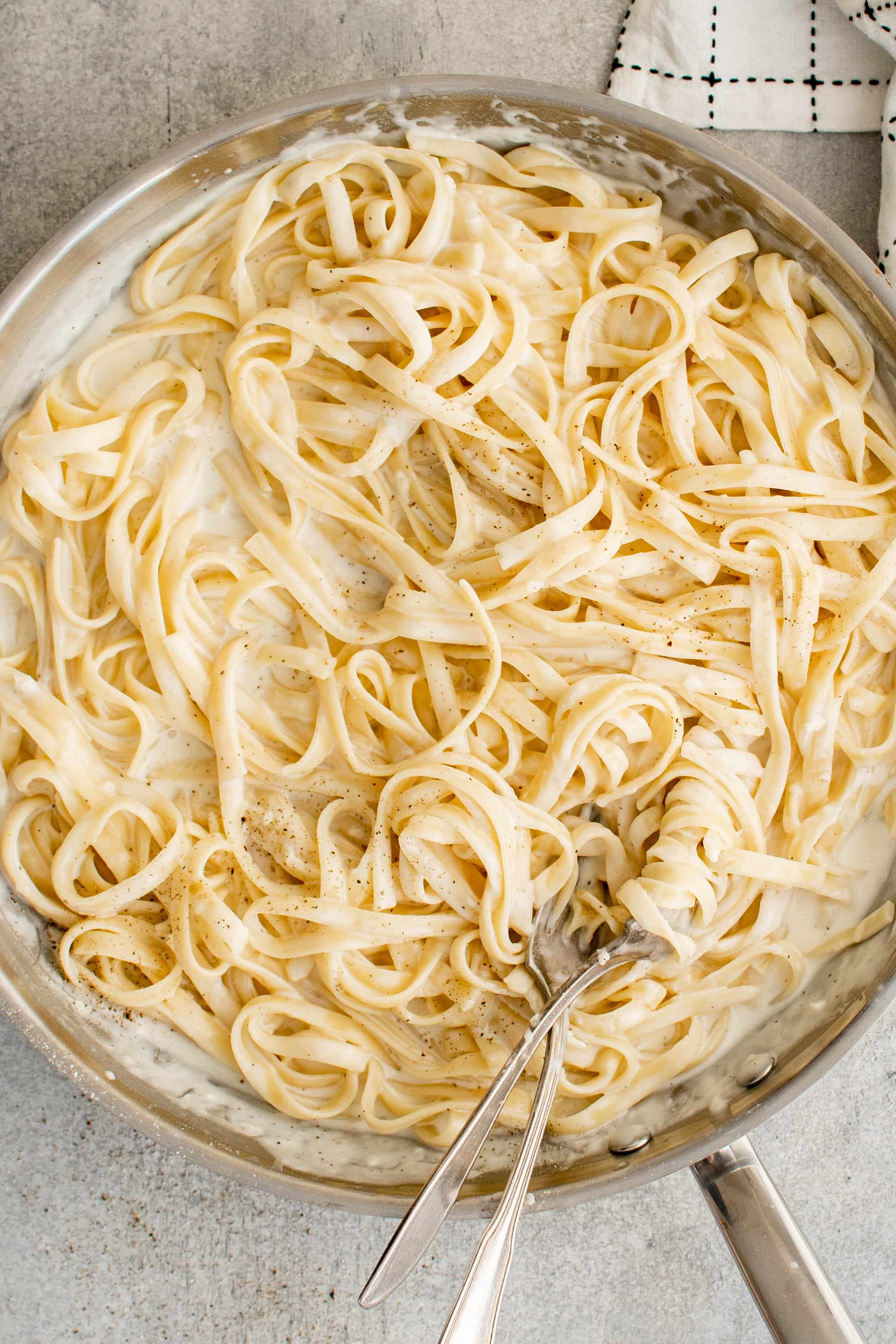 Large stainless steel skillet filled with cooked fettuccine noodles tossed in alfredo sauce.
