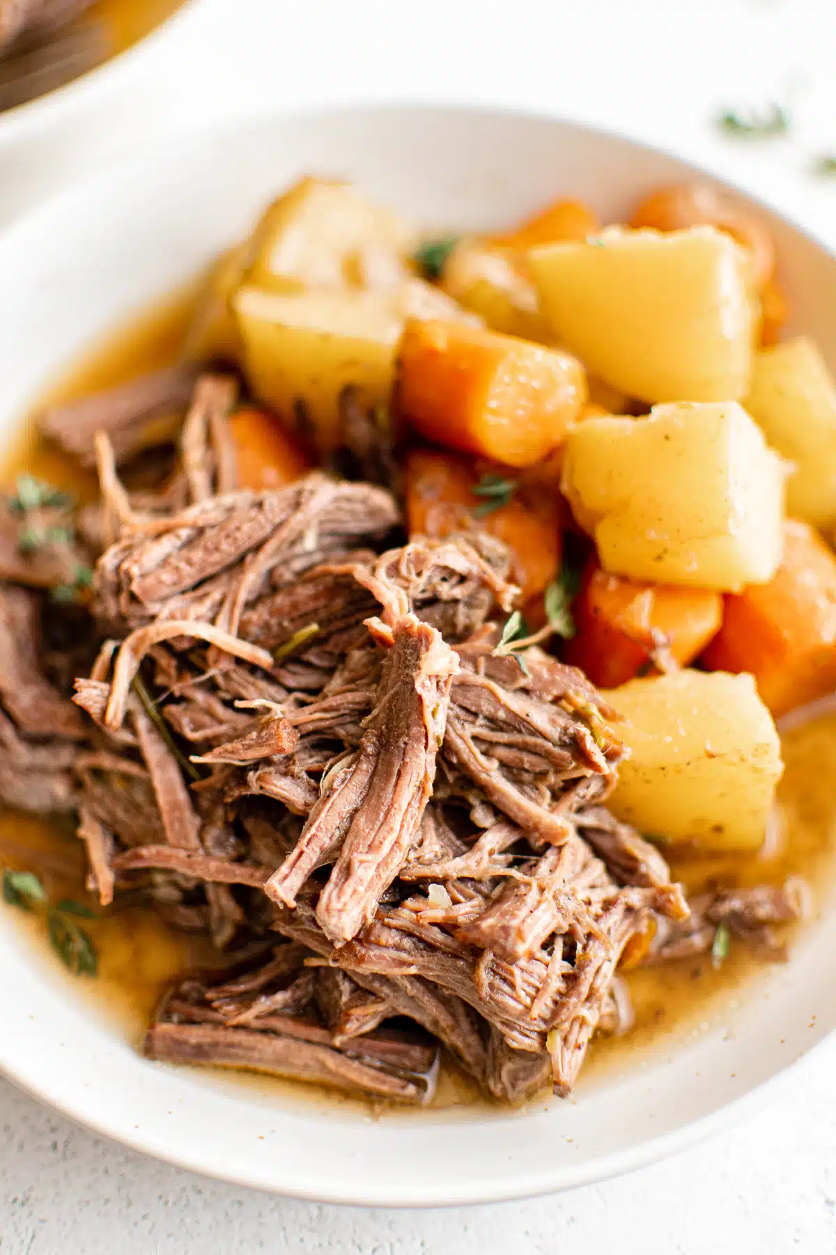 White dinner plate with a serving of shredded beef pot roast and a side of stewed carrots, onions, and potatoes.