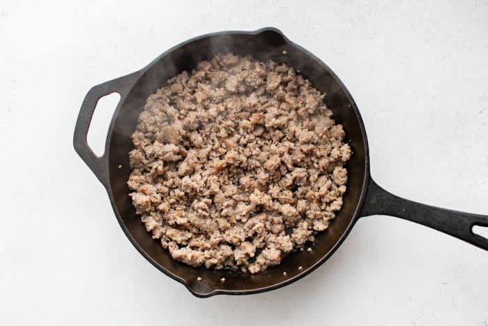 Browned crumbled breakfast sausage sizzling in a cast-iron skillet.