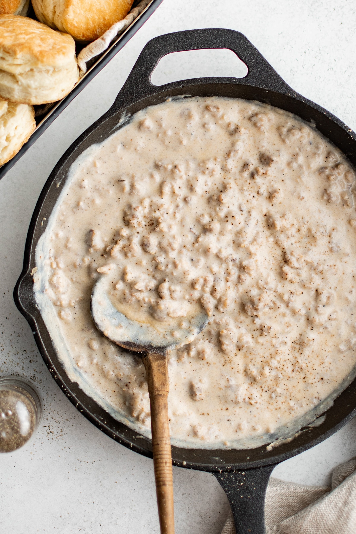 Sausage gravy in a cast-iron skillet with a wooden ladle, biscuits visible on the side.