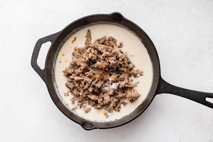 Browned sausage with seasonings added back into creamy roux in a skillet.