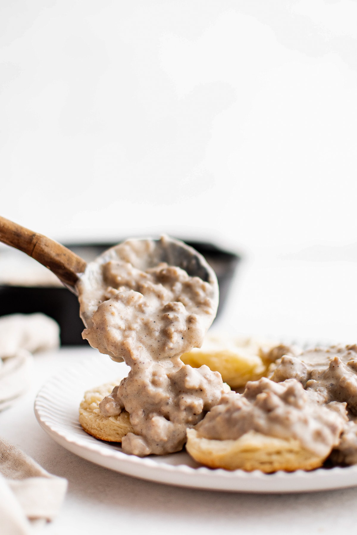 Wooden ladle pouring creamy sausage gravy over split homemade biscuits on a plate.