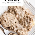 Southern-style sausage gravy poured over fluffy homemade biscuits on a white plate with a fork.