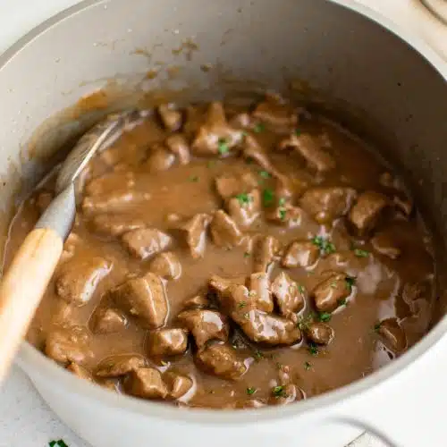Large white pot filled with simmering beef tips in gravy.