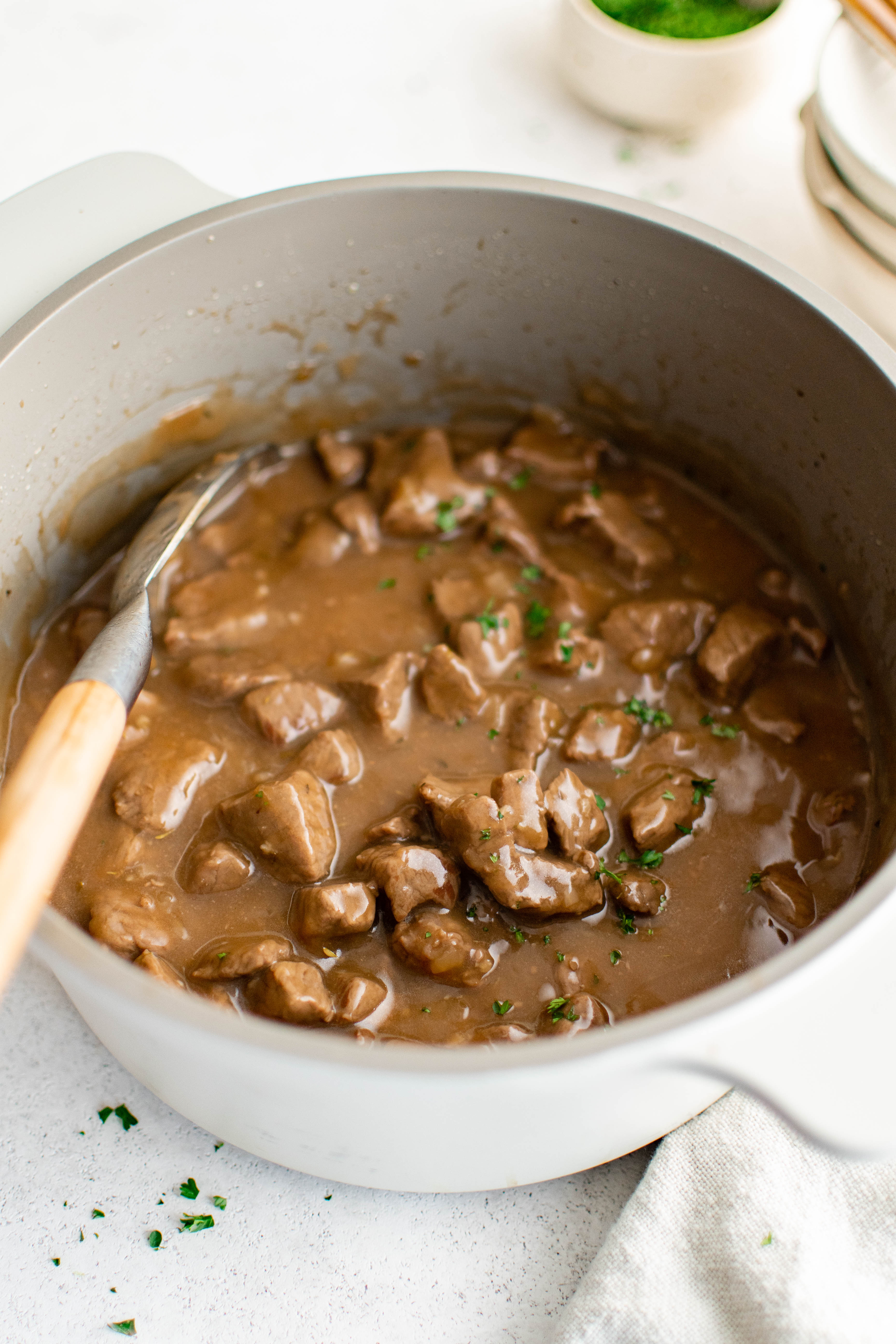 Large white pot filled with simmering beef tips in gravy.