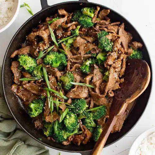 Cast iron skillet filled with cooked beef and broccoli recipe garnished with slice green onions.