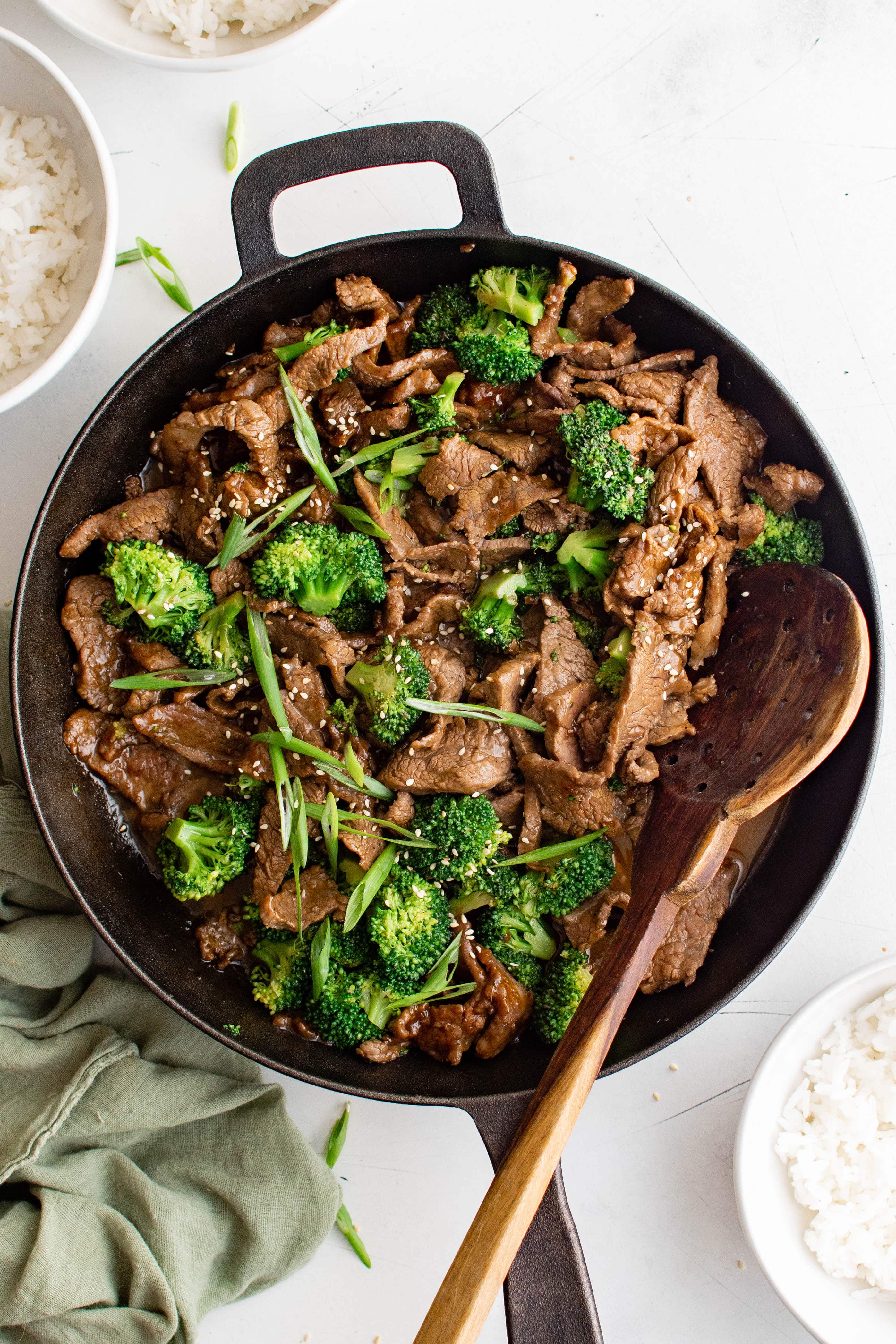 Cast iron skillet filled with cooked beef and broccoli recipe garnished with slice green onions.