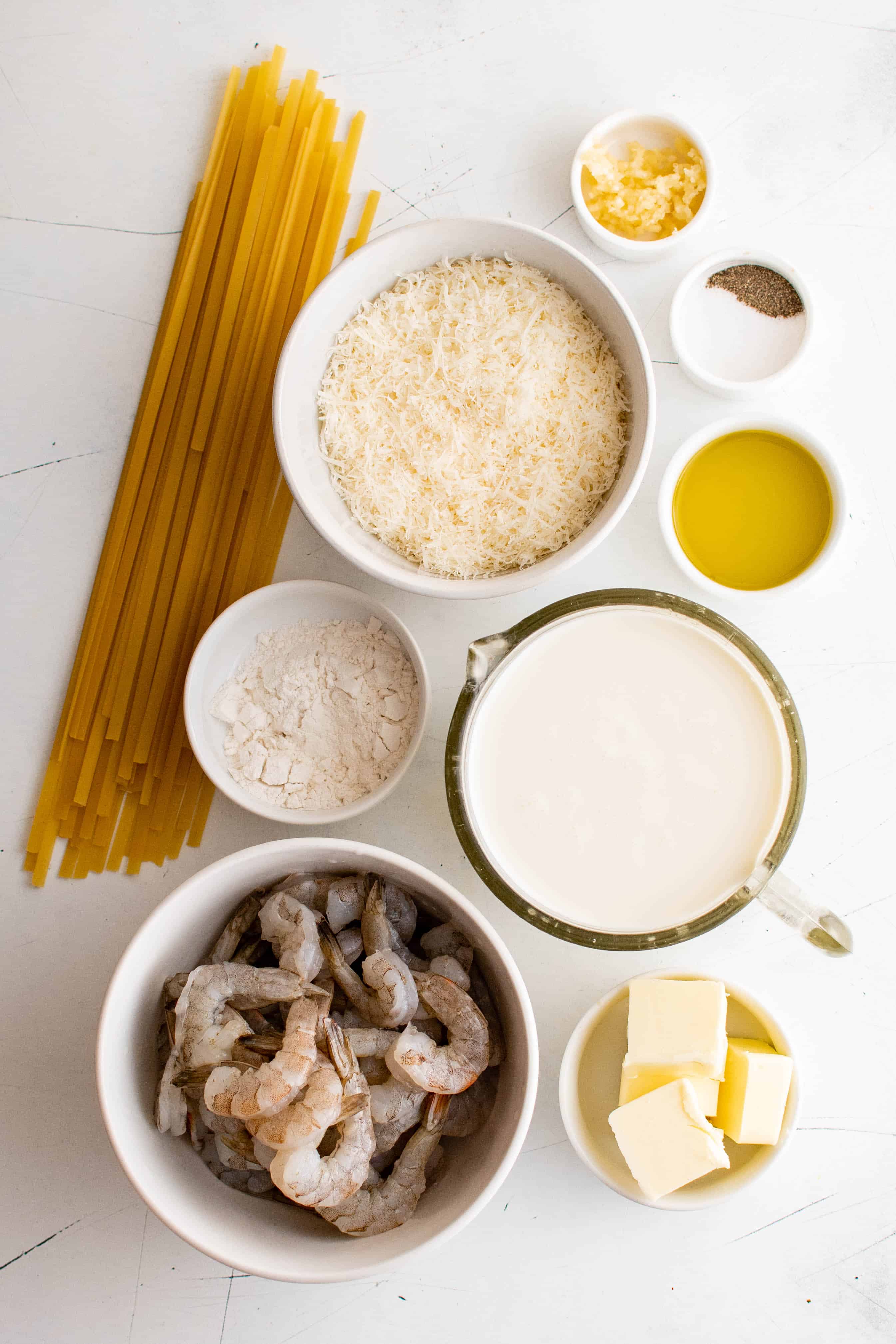 Ingredients for shrimp alfredo pasta set aside in individual serving bowls.