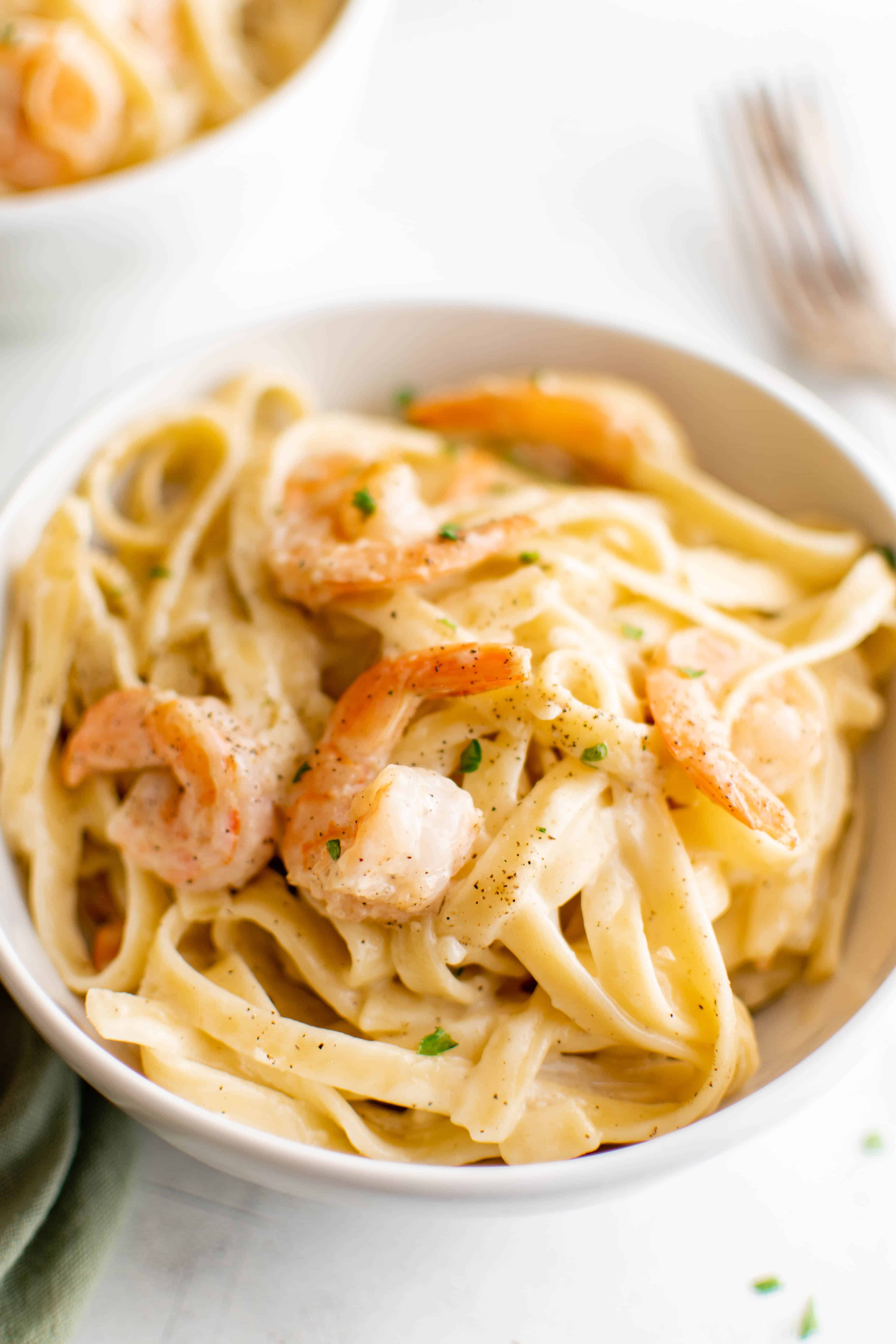 White bowl filled with shrimp alfredo pasta and garnished with chopped parsley.