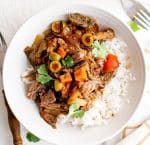 Slow cooker picadillo pot roast with tender beef, olives, tomatoes, and bell peppers served over white rice and garnished with fresh cilantro.