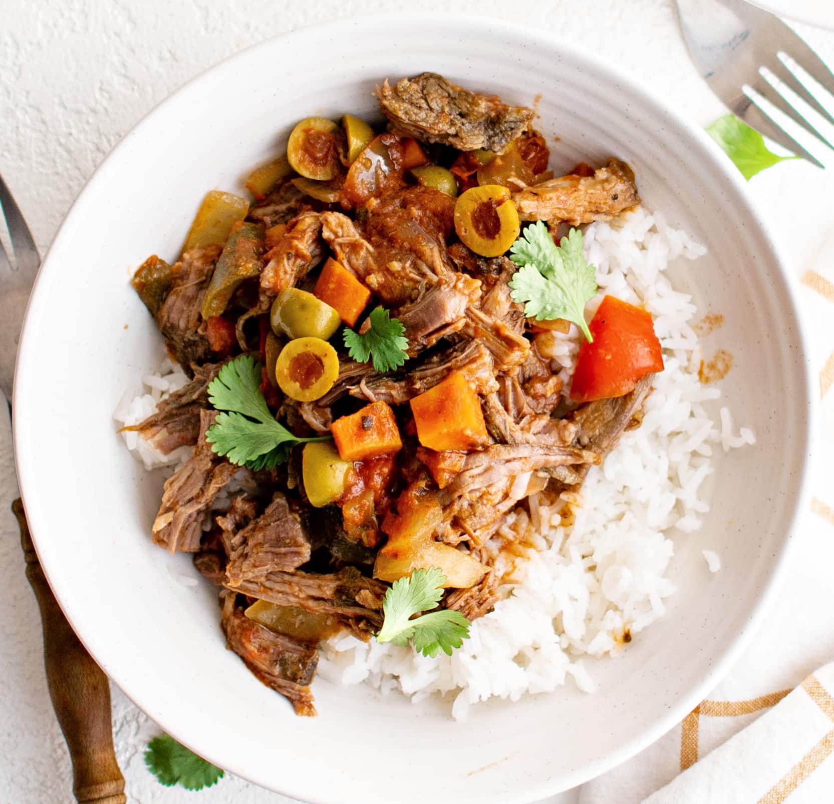 Slow cooker picadillo pot roast with tender beef, olives, tomatoes, and bell peppers served over white rice and garnished with fresh cilantro.