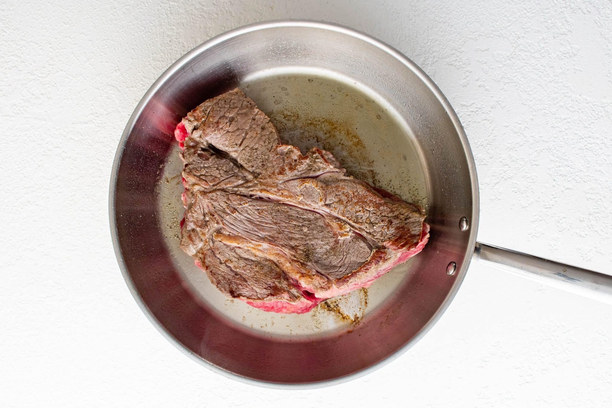 Browned chuck roast in a large stainless steel skillet.