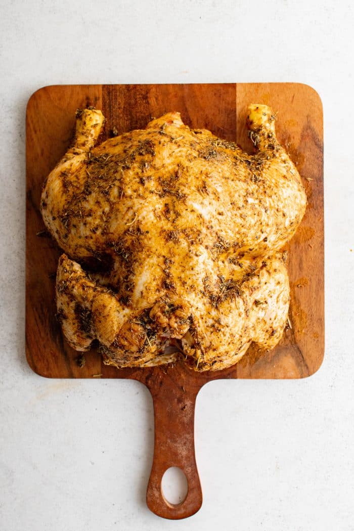 Whole chicken on a cutting board completely coated in homemade poultry seasoning and olive oil.