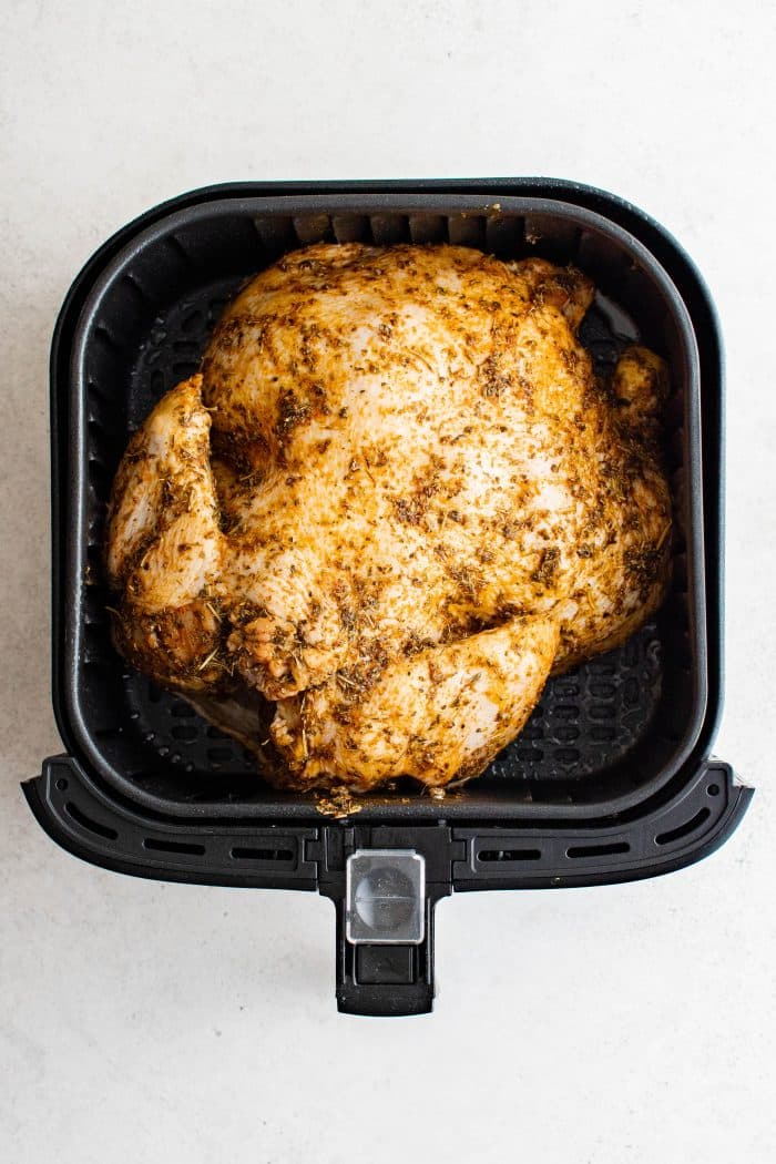 Seasoned raw whole chicken breast-side-down in the basket of an air fryer.