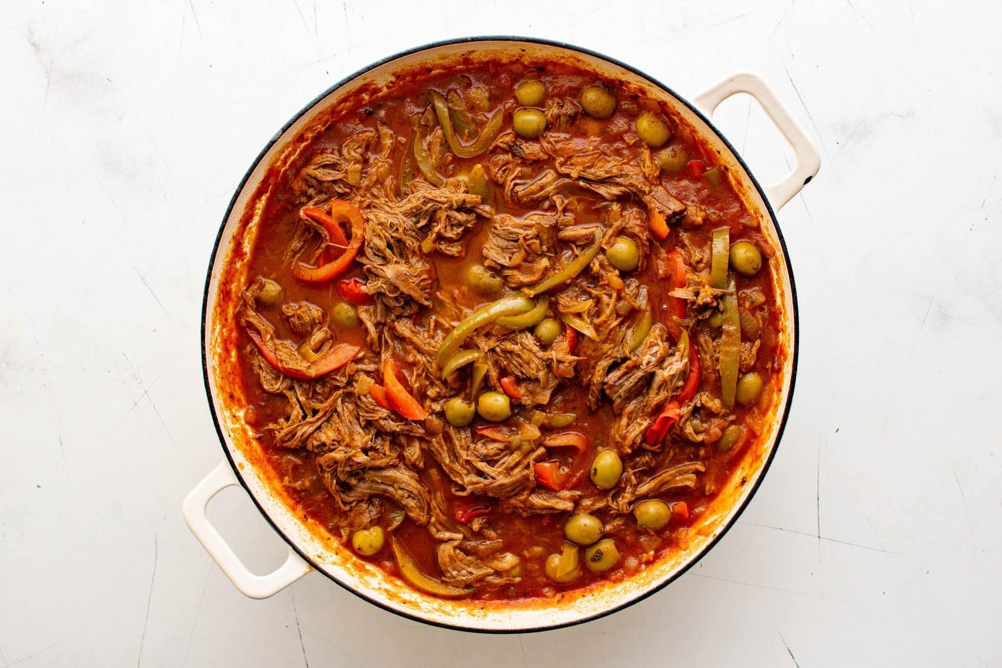 Finished ropa vieja with shredded beef, peppers, and olives in a white Dutch oven.