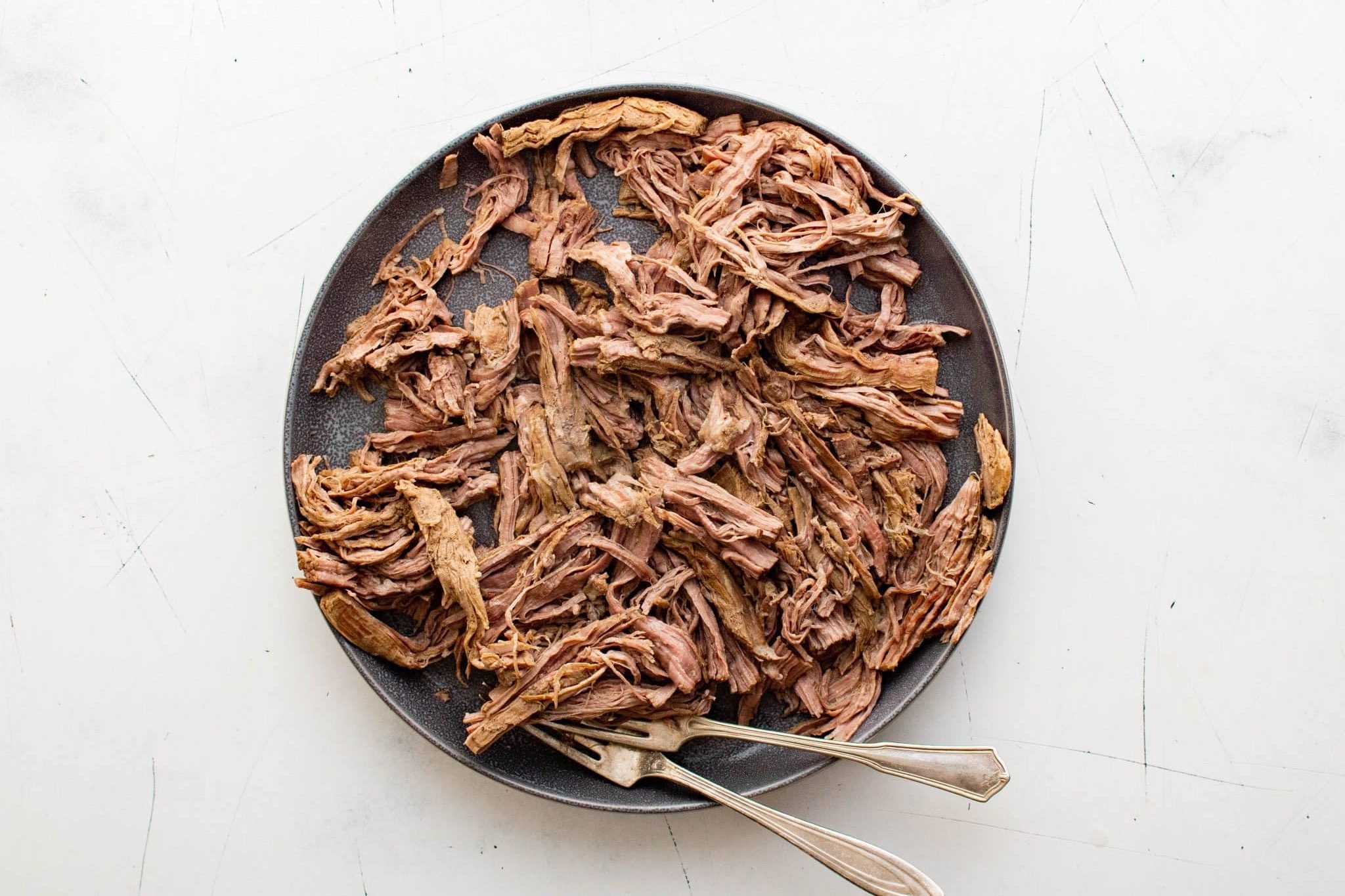Plate of shredded flank steak with two forks ready for making ropa vieja.