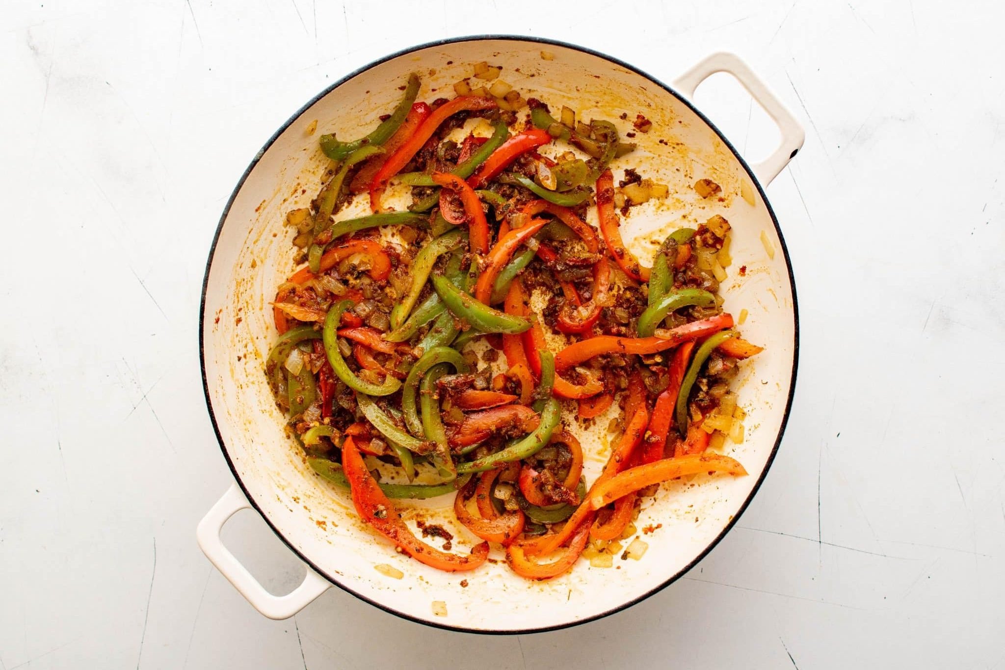 Cooked peppers and onions coated with tomato paste and spices in a skillet.