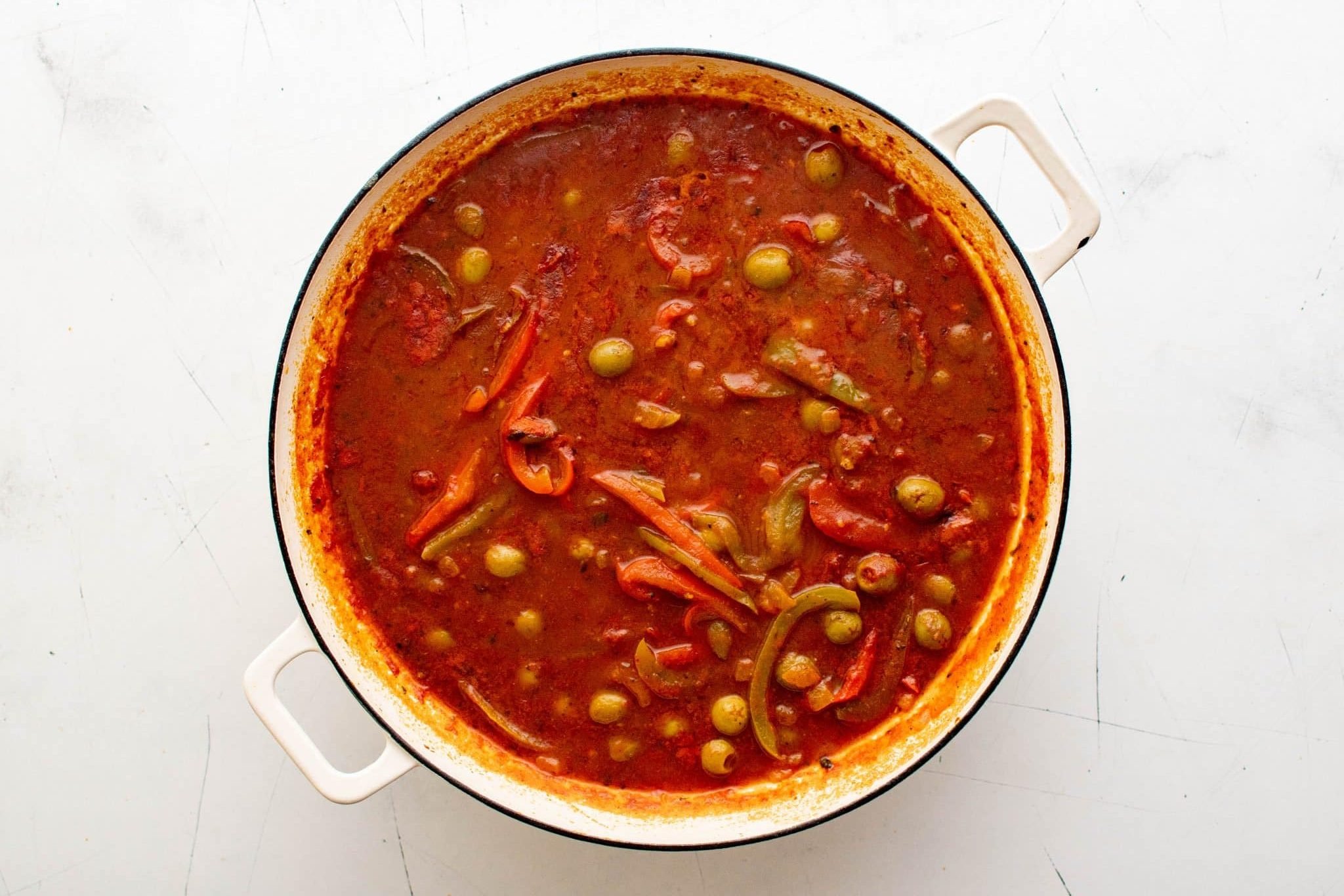 Dutch oven filled with tomato sauce, peppers, and green olives simmering for ropa vieja.