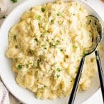A large white bowl filled with creamy potato salad and garnished with chopped parsley.