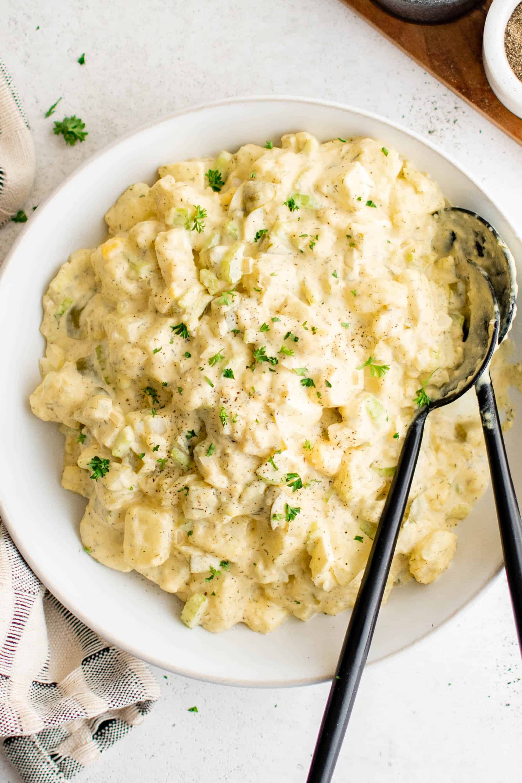 A large white bowl filled with creamy potato salad and garnished with chopped parsley.