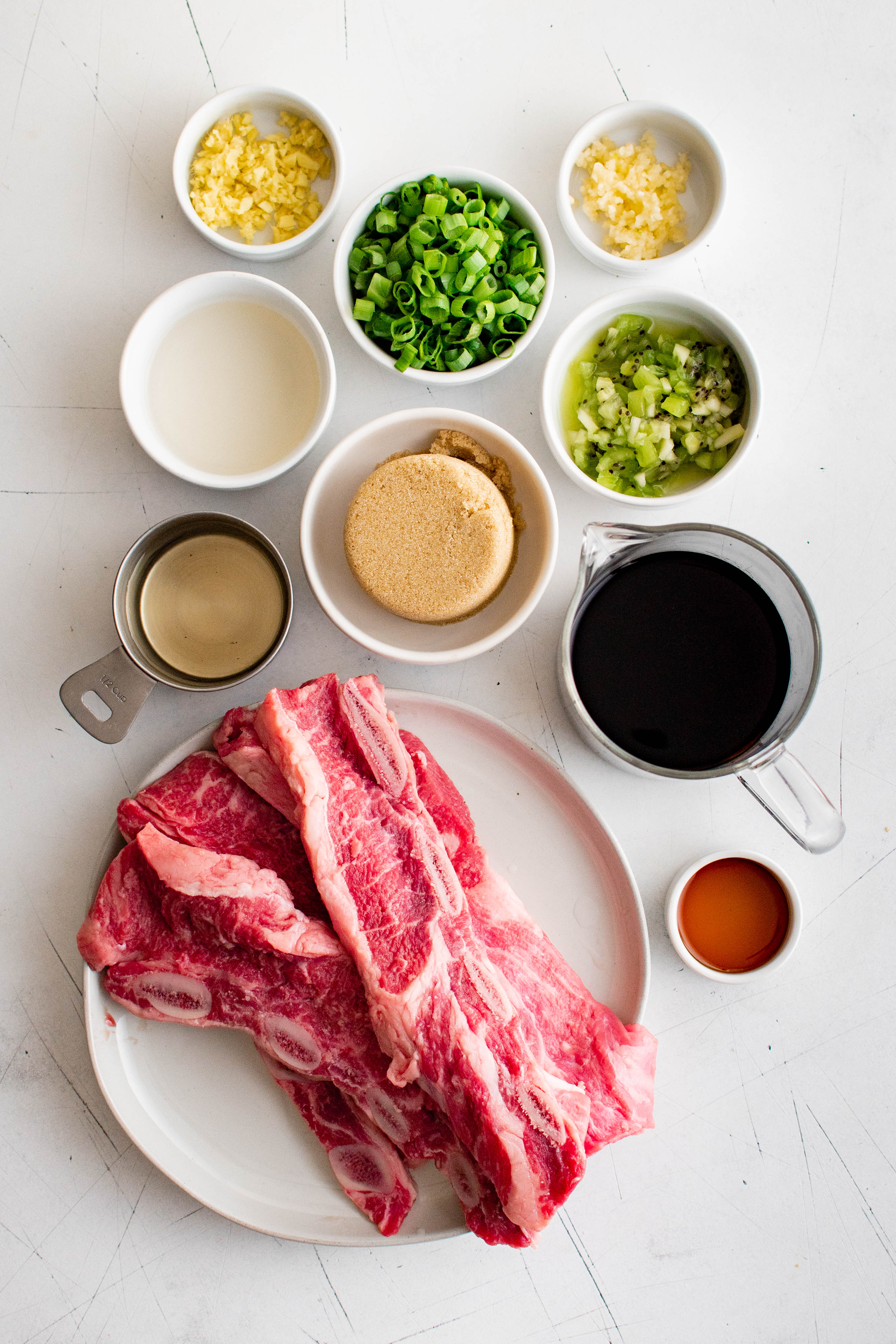 Ingredients needed to make Kalbi (Korean BBQ Beef Short Ribs) set aside in individual serving bowls.